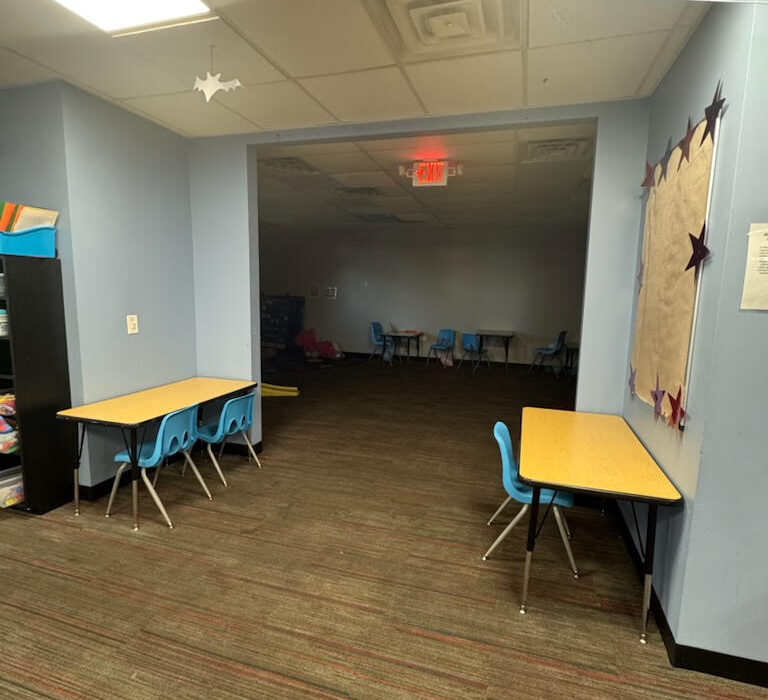 show the interior of a classroom or child care center hallway with soft blue walls, laminate tables with yellow tops