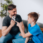A father practicing speech sounds at home with his young son using a letter of the alphabet.