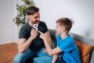 A father practicing speech sounds at home with his young son using a letter of the alphabet.