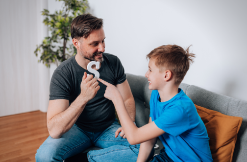 A father practicing speech sounds at home with his young son using a letter of the alphabet.