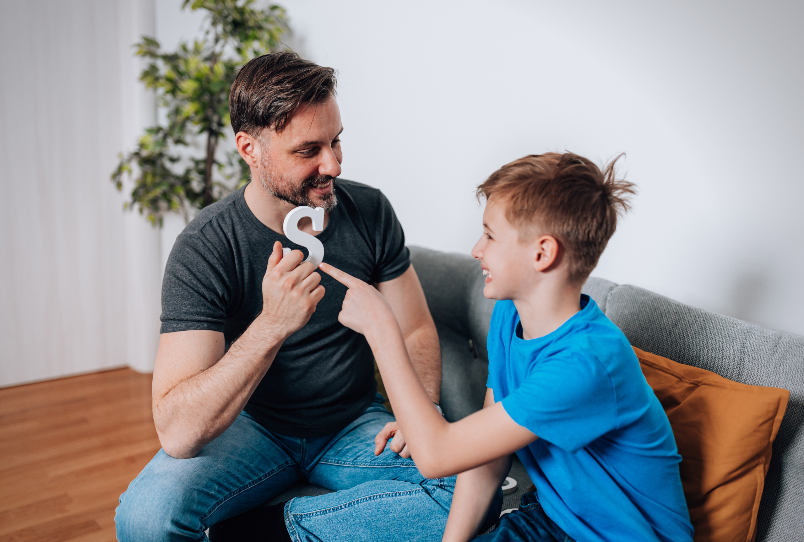 A father practicing speech sounds at home with his young son using a letter of the alphabet.