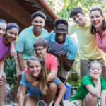 A diverse group of children with disabilities and a camp counselor smiling together at an inclusive summer camp near Chicago.