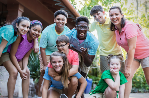 A diverse group of children with disabilities and a camp counselor smiling together at an inclusive summer camp near Chicago.