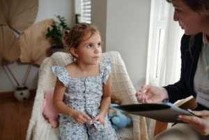 A young girl sitting attentively during a speech-language evaluation with a pediatric therapist taking notes.