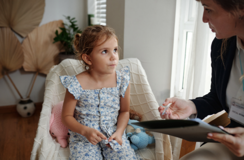 A young girl sitting attentively during a speech-language evaluation with a pediatric therapist taking notes.