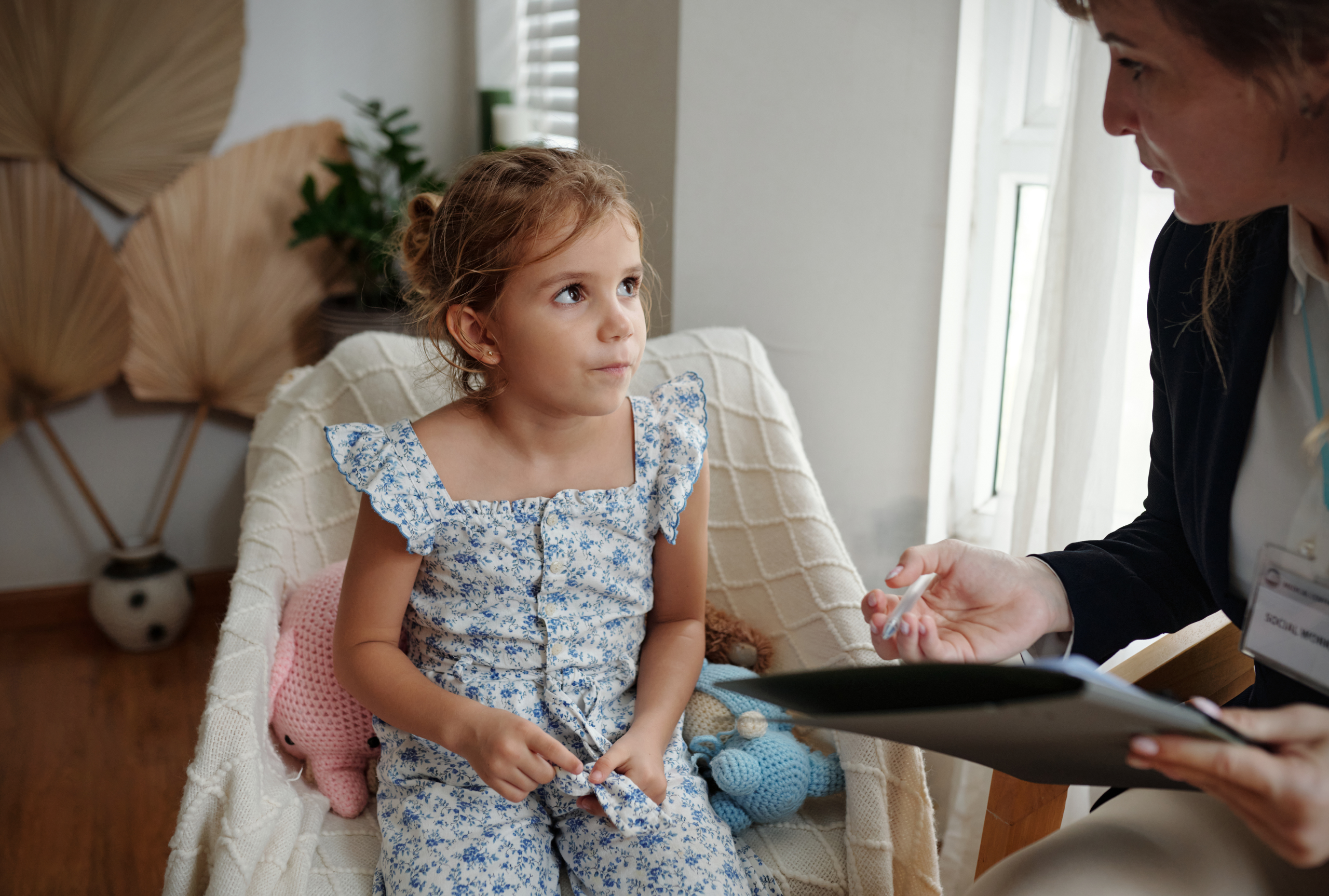 A young girl sitting attentively during a speech-language evaluation with a pediatric therapist taking notes.