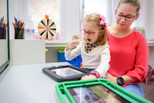 A speech therapist working with a young girl using a tablet during a pediatric speech therapy session.