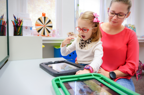 A speech therapist working with a young girl using a tablet during a pediatric speech therapy session.