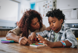 A mother supporting her child with autism during a puzzle activity at home, representing autism caregiver mental health awareness.