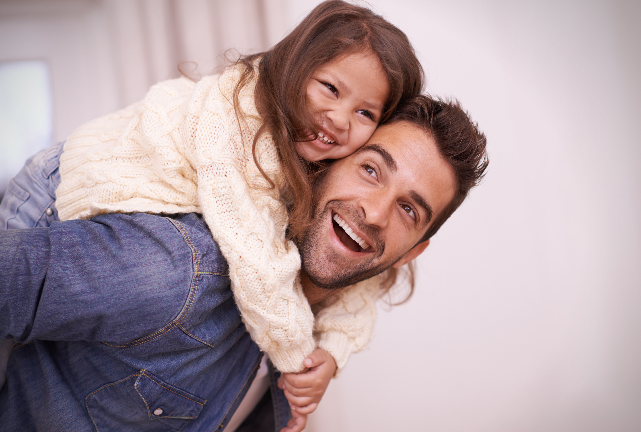 A father laughing and giving his young daughter a piggyback ride at home, representing dad involvement in children's therapy support.