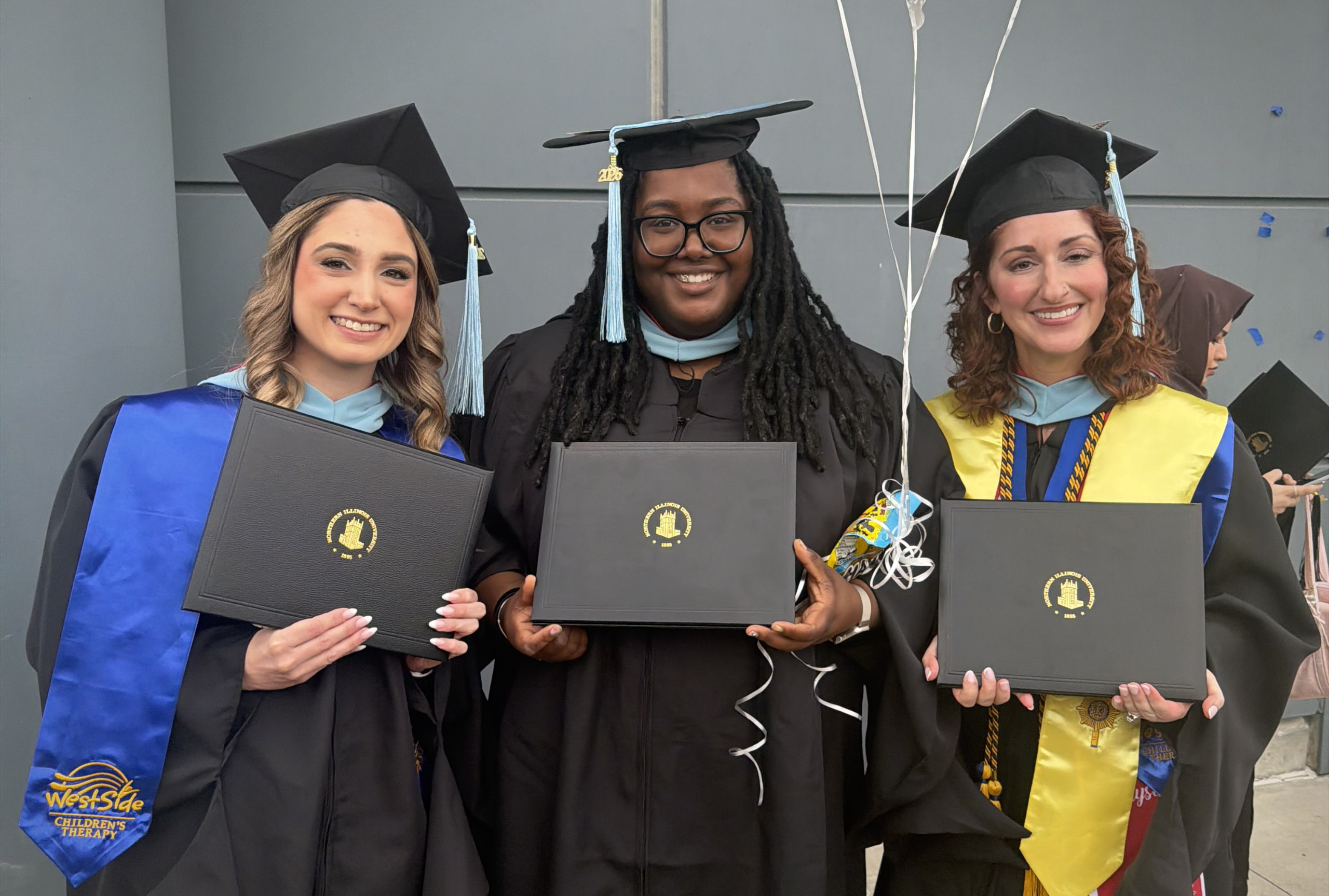 Three Westside Children's Therapy RBTs in graduation caps and gowns holding NIU diplomas after completing the Westside NIU BCBA cohort program.