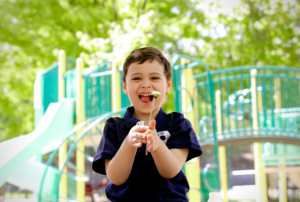A young boy with autism smiling and playing outdoors at a playground during summer.