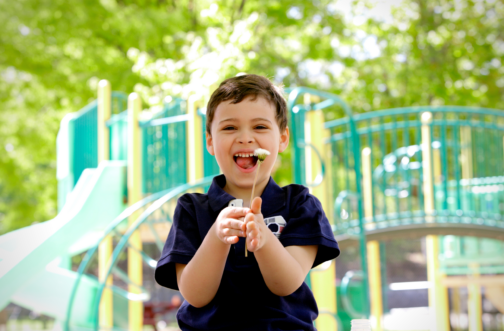 A young boy with autism smiling and playing outdoors at a playground during summer.
