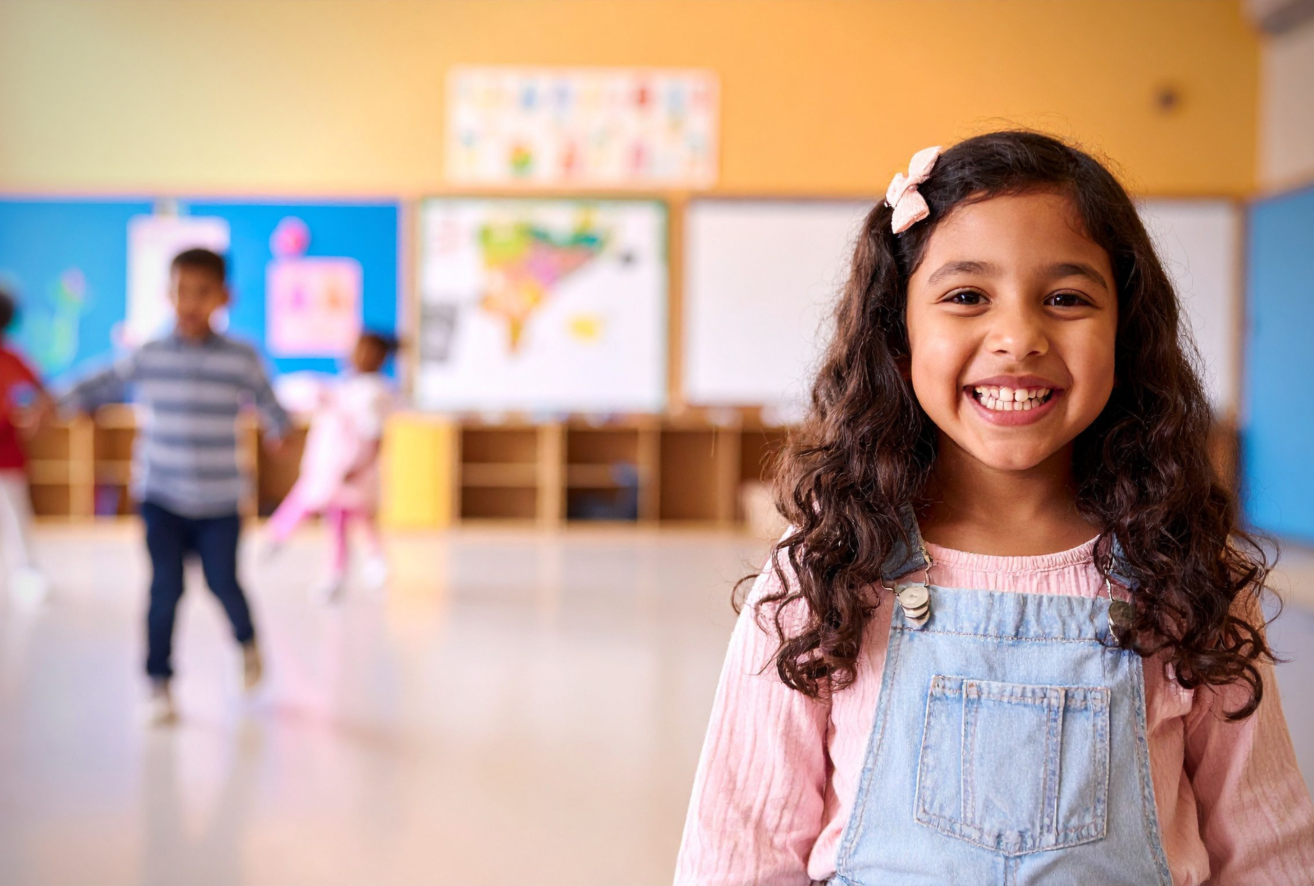 A young girl smiling confidently in a preschool classroom, representing school readiness skills built through ABA therapy for children with autism.