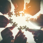 Circle of hands connecting puzzle pieces together, representing interdisciplinary care team collaboration
