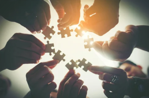Circle of hands connecting puzzle pieces together, representing interdisciplinary care team collaboration