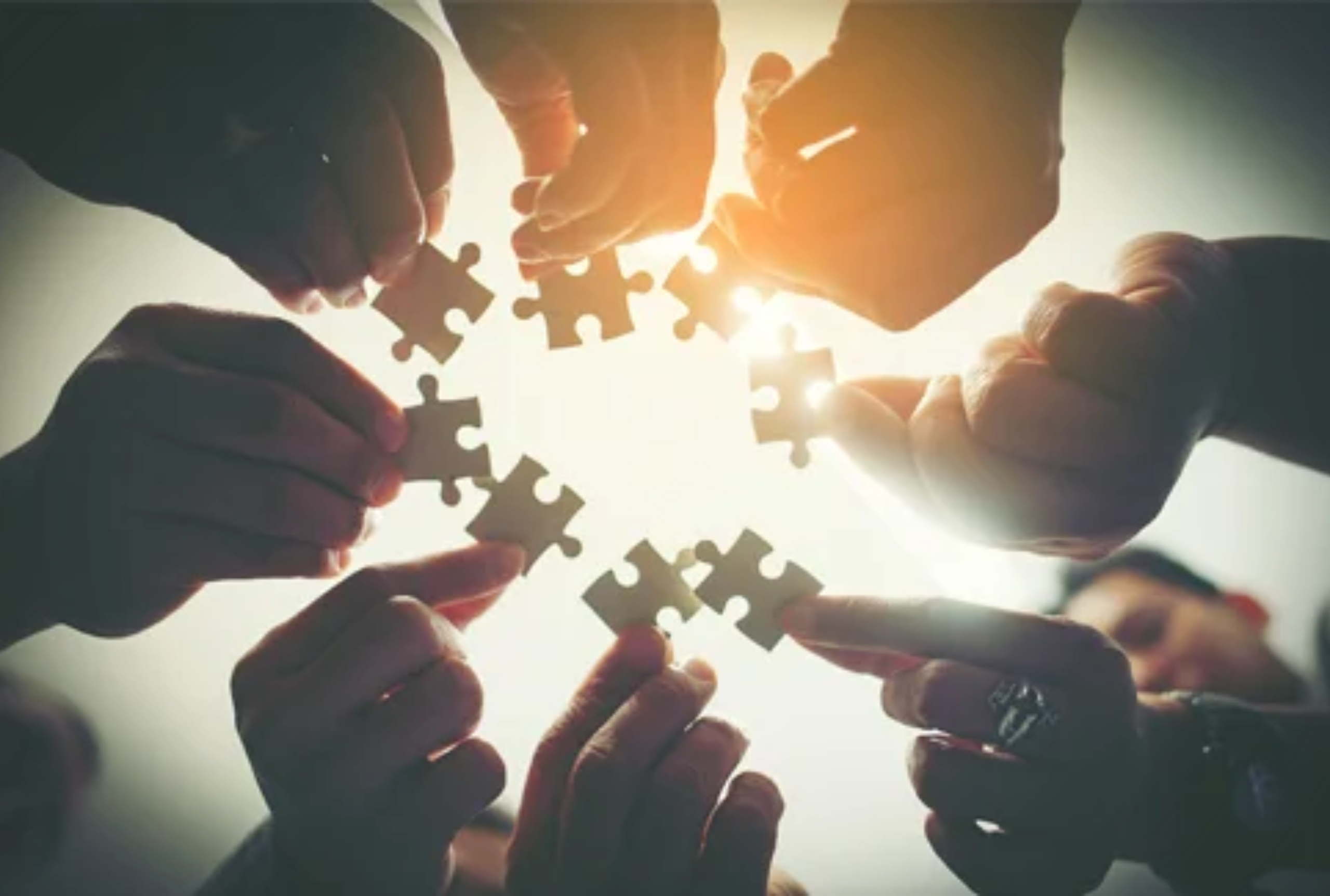 Circle of hands connecting puzzle pieces together, representing interdisciplinary care team collaboration