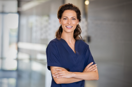 Smiling female clinician in navy scrubs standing confidently with arms crossed in a clinic hallway