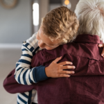 A young boy hugs his grandfather tightly, his head resting against his grandfather's shoulder.