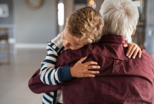 A young boy hugs his grandfather tightly, his head resting against his grandfather's shoulder.