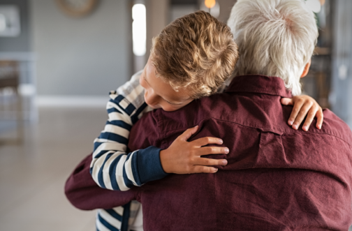 A young boy hugs his grandfather tightly, his head resting against his grandfather's shoulder.