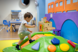 A toddler in socks carefully climbs over a colorful padded play structure at an indoor children's gym.