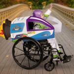 A child in a space ranger costume cheers with a raised fist while seated in a wheelchair transformed into a spaceship with a costume cover, representing adaptive Halloween costume ideas for kids who use wheelchairs.