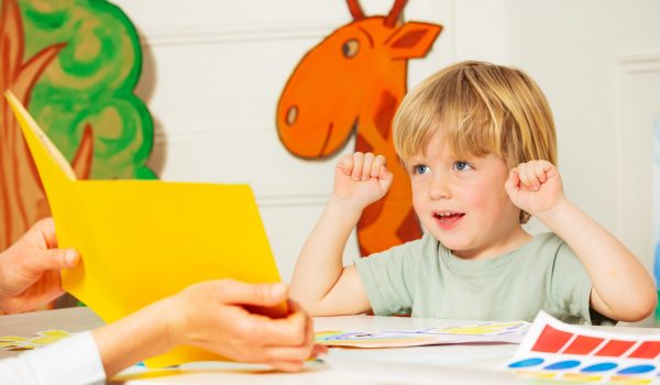Early development lesson - little blond boy engaged in the process lift hands looking at the picture in the book